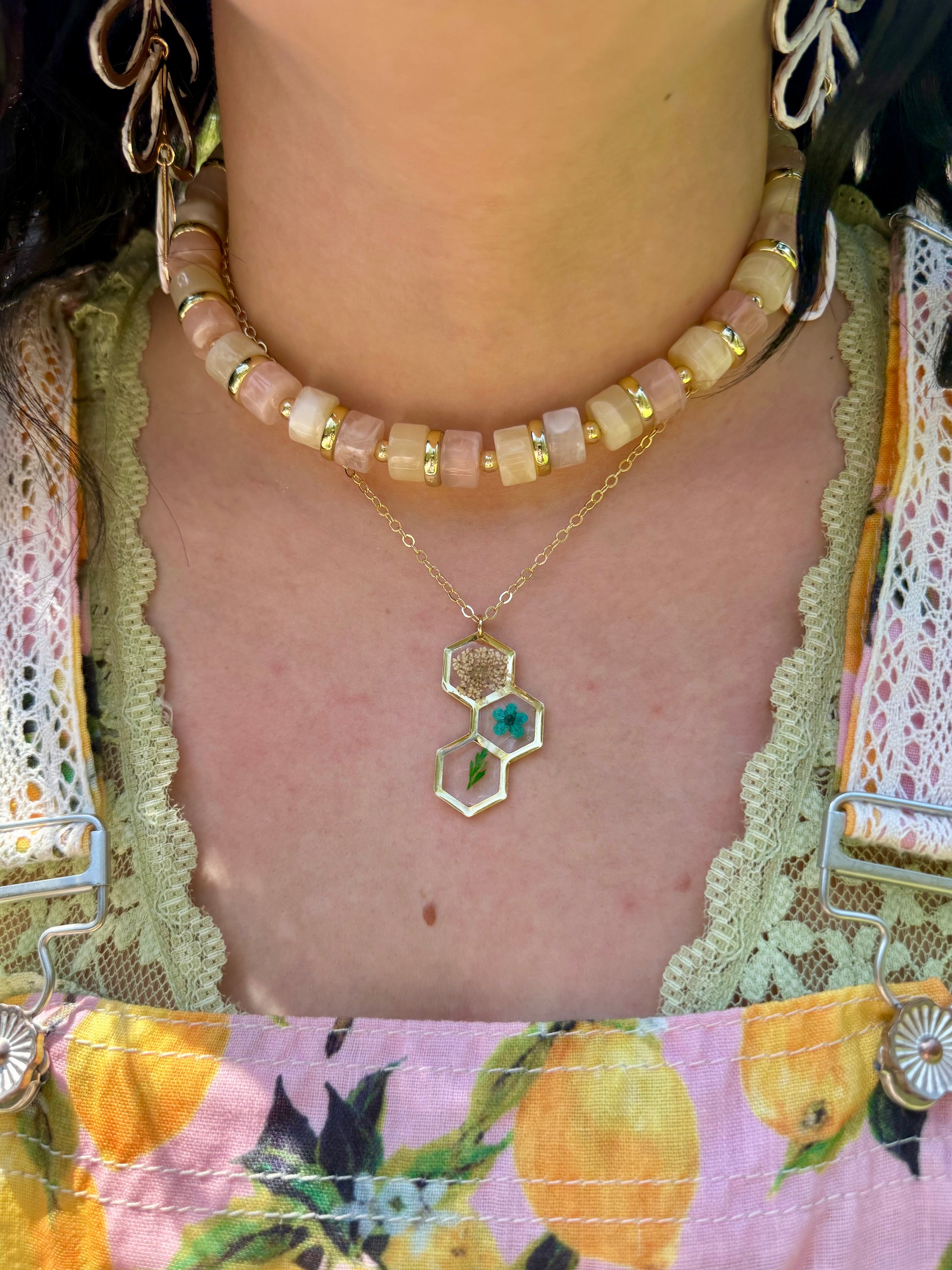 Close-up of a person wearing a gold necklace with a hexagonal pendant, surrounded by colorful clothing.