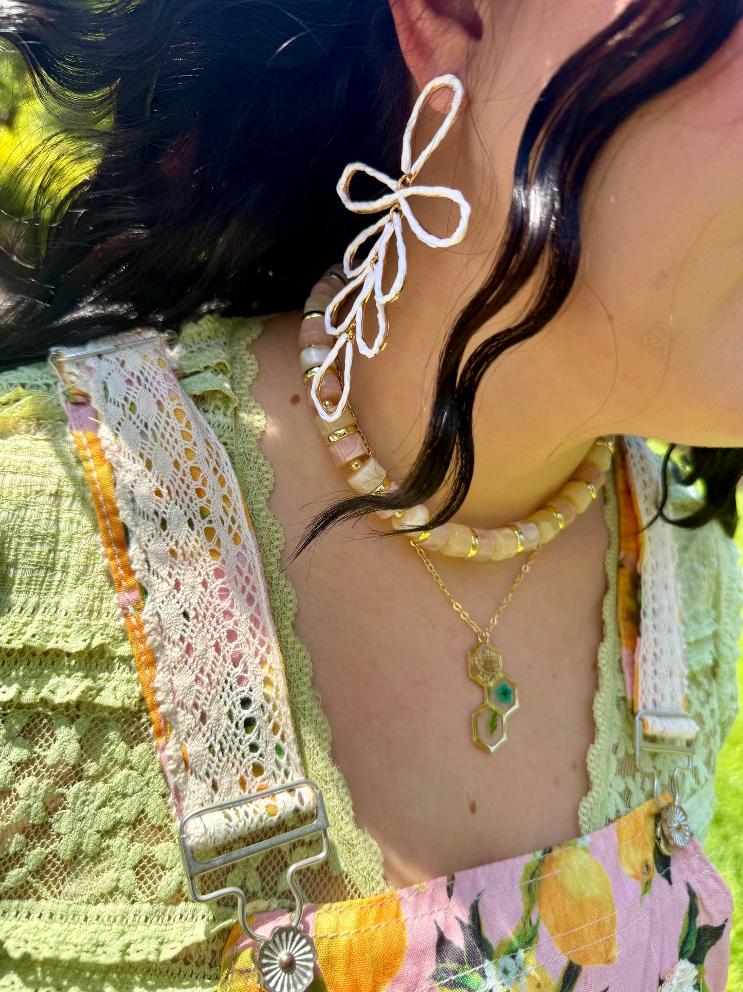 Close-up of a person wearing a floral top with lace details, a necklace, and earrings.