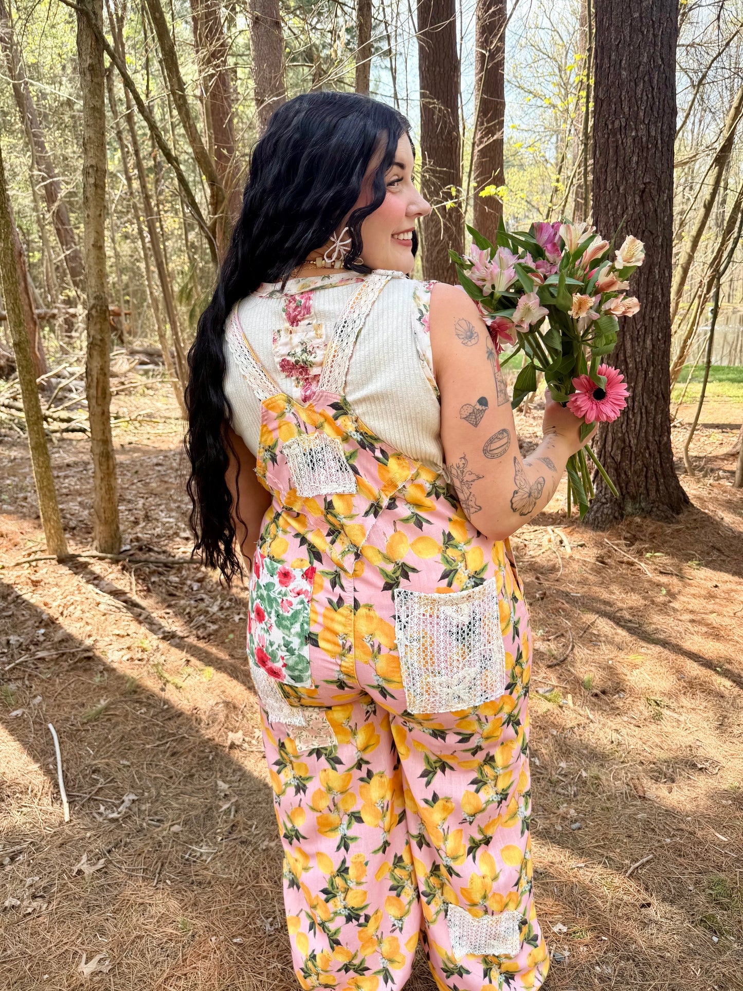 Woman in a floral overalls holding flowers in a forest setting