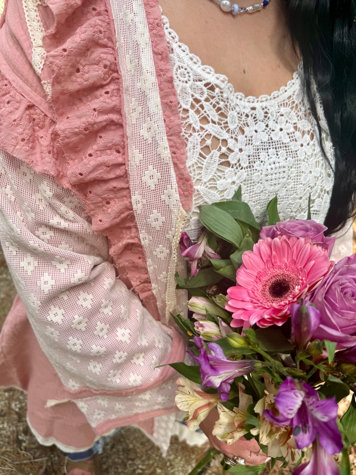 Person wearing a pink lace dress holding a bouquet of flowers outdoors
