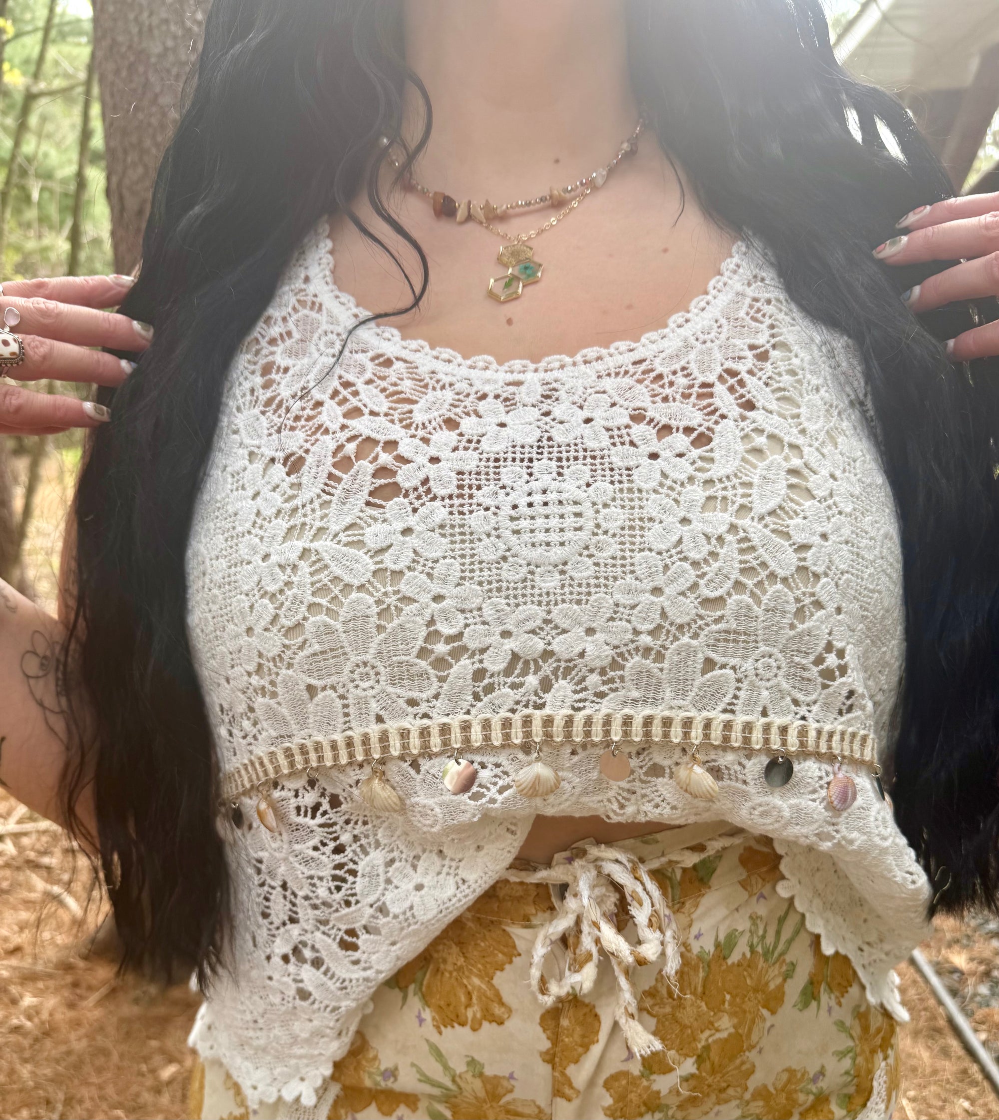 Person wearing a white lace top with a forest background