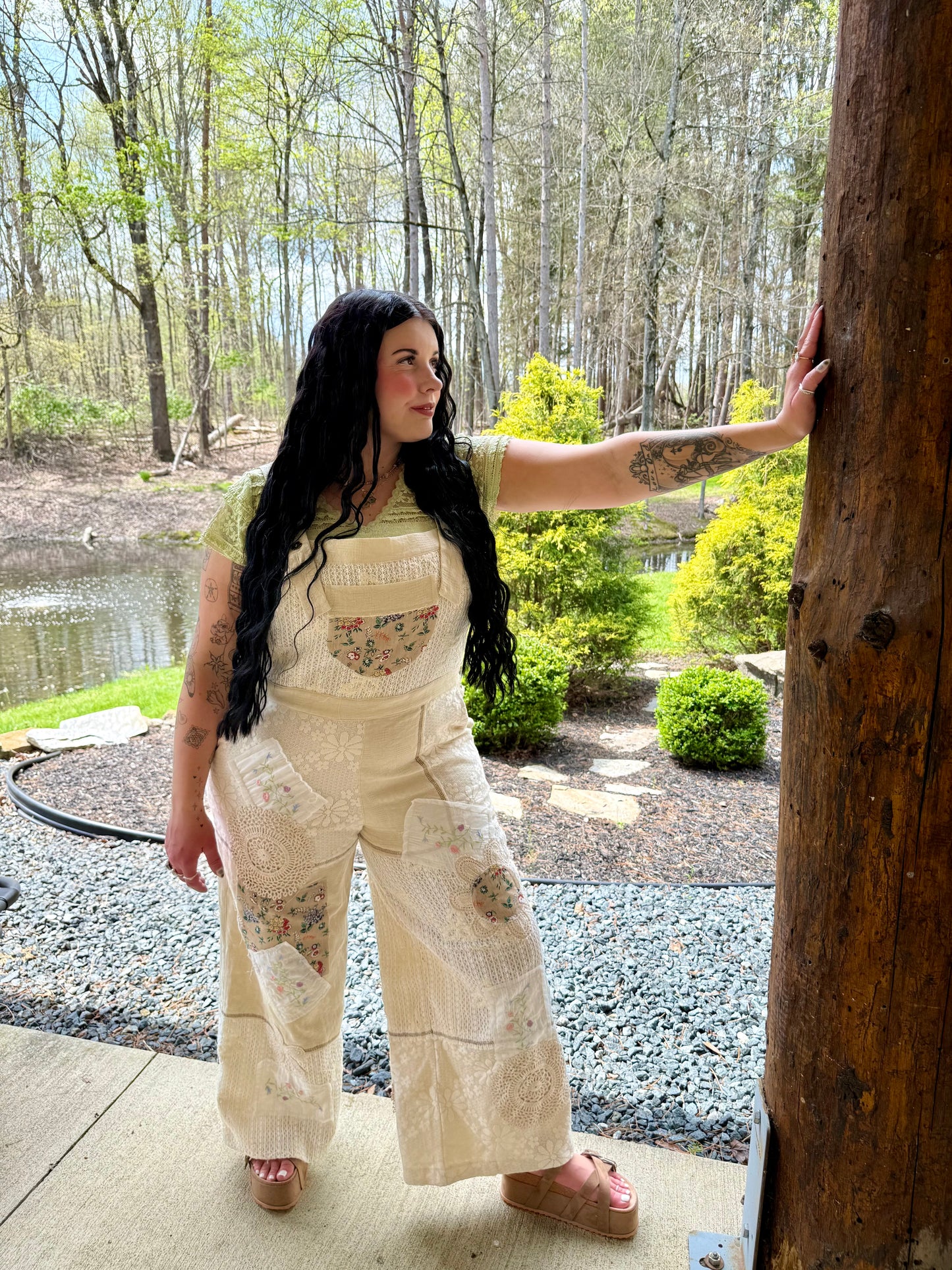 Woman in a floral overalls standing by a wooden post with a natural landscape in the background