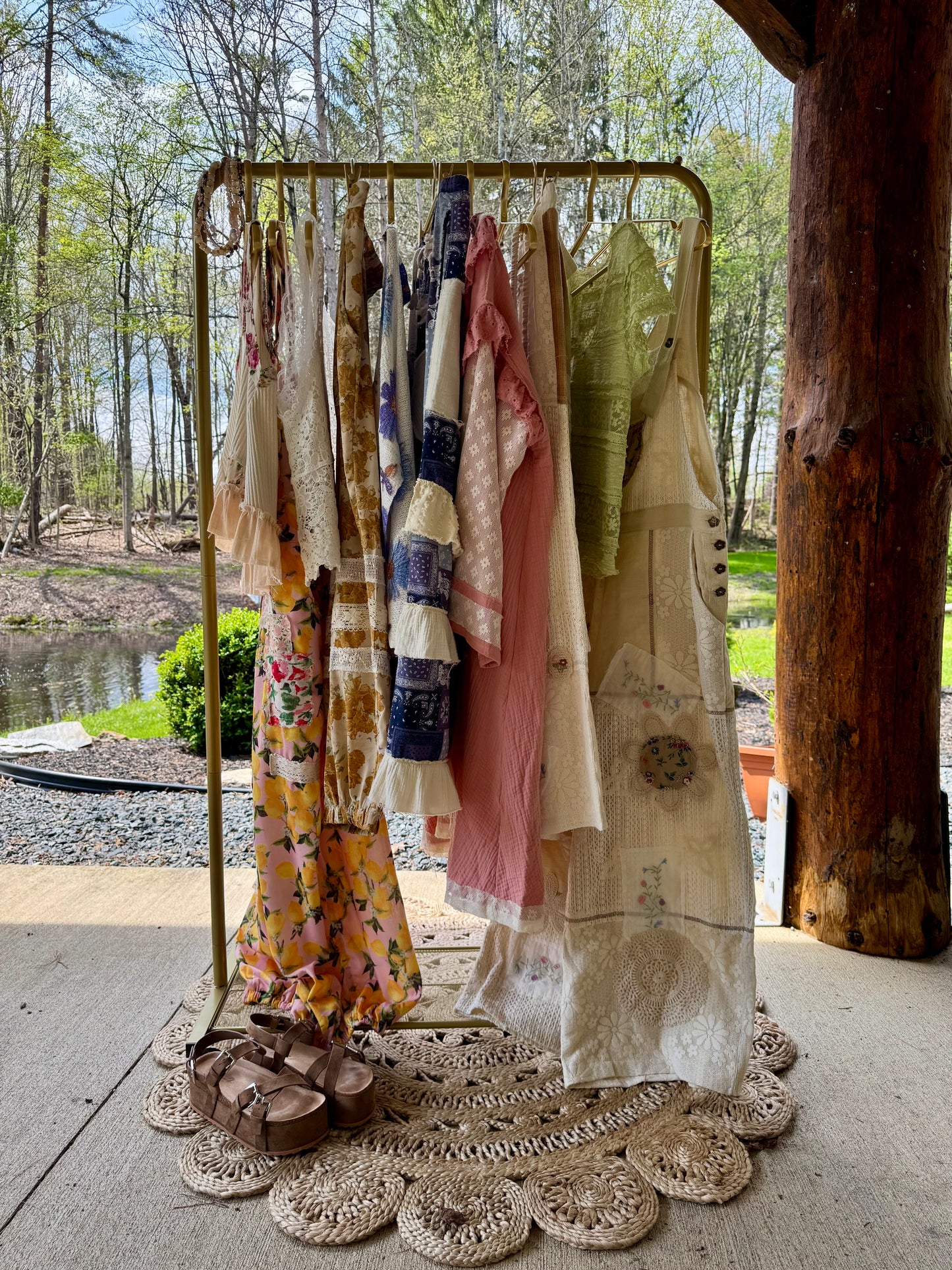 Clothing rack with various garments outdoors near a body of water and trees.