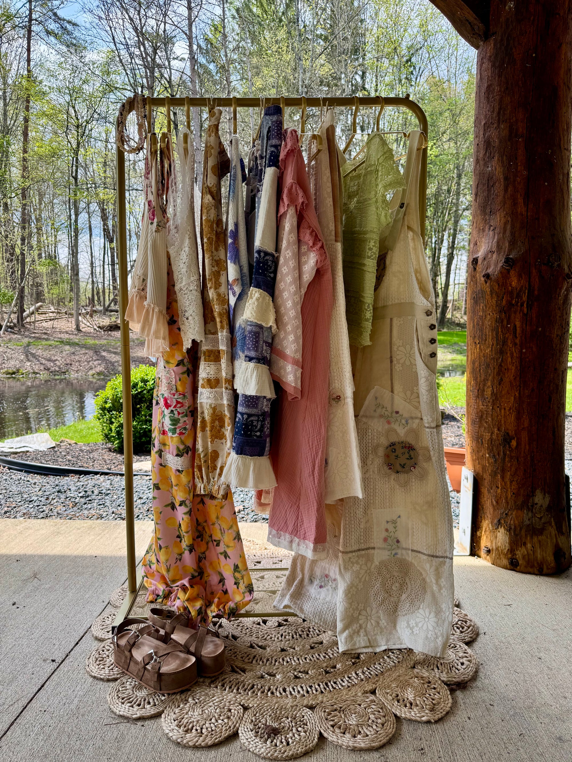 Clothing rack with various garments outdoors near a body of water and trees.