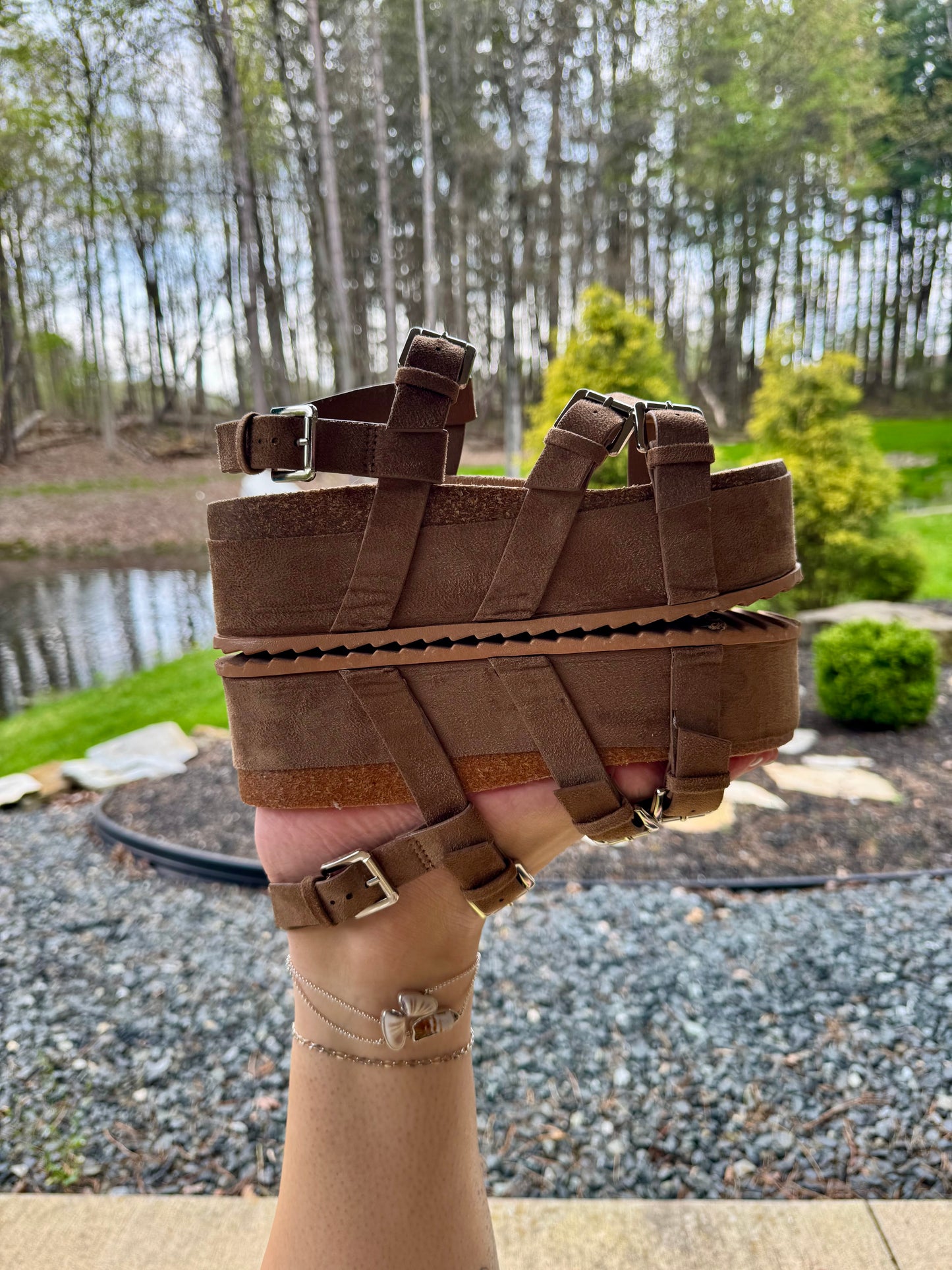 Brown woven sandal held up with a natural outdoor background