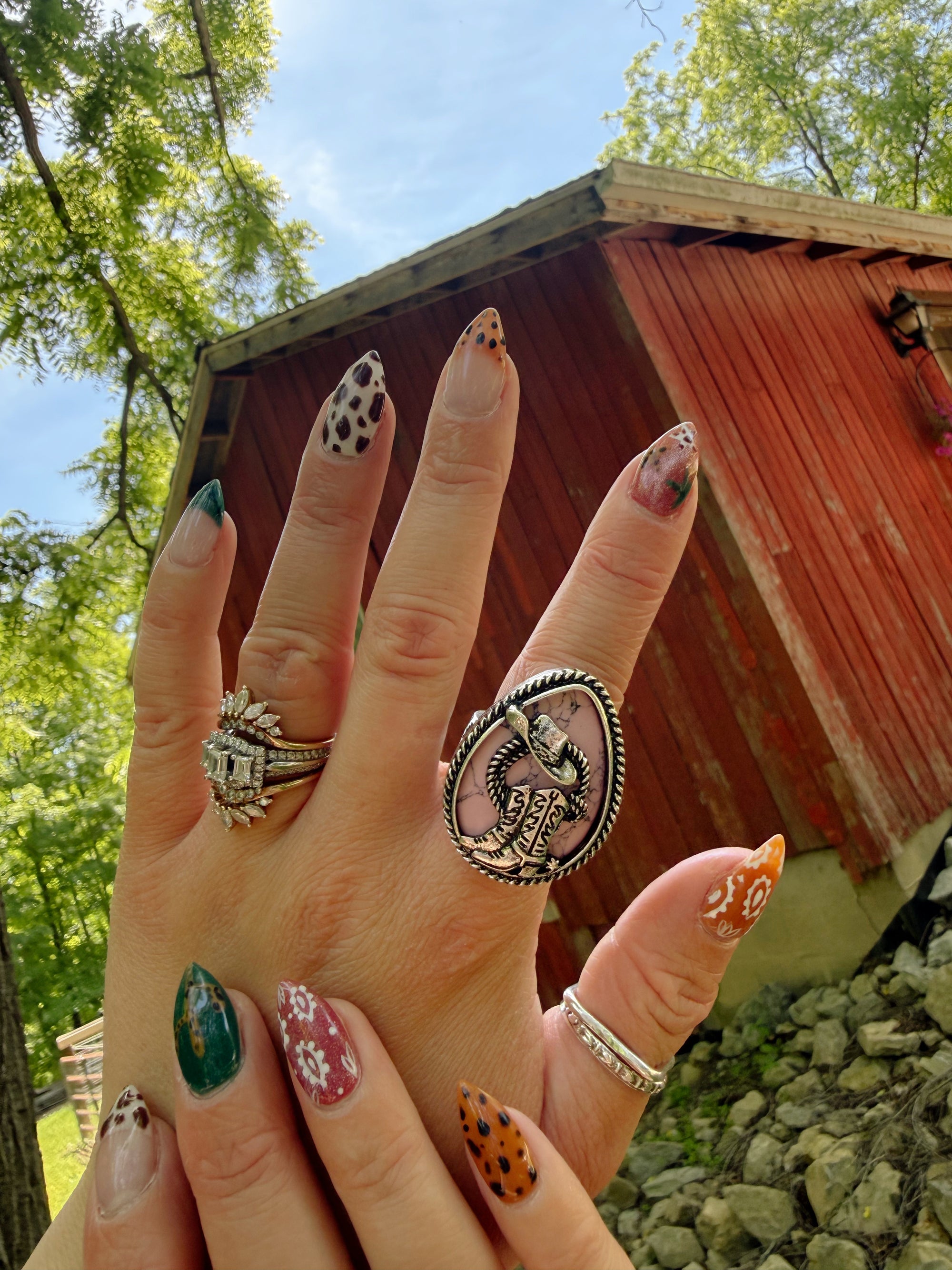 Hand with decorated nails and rings in front of a red wooden structure.