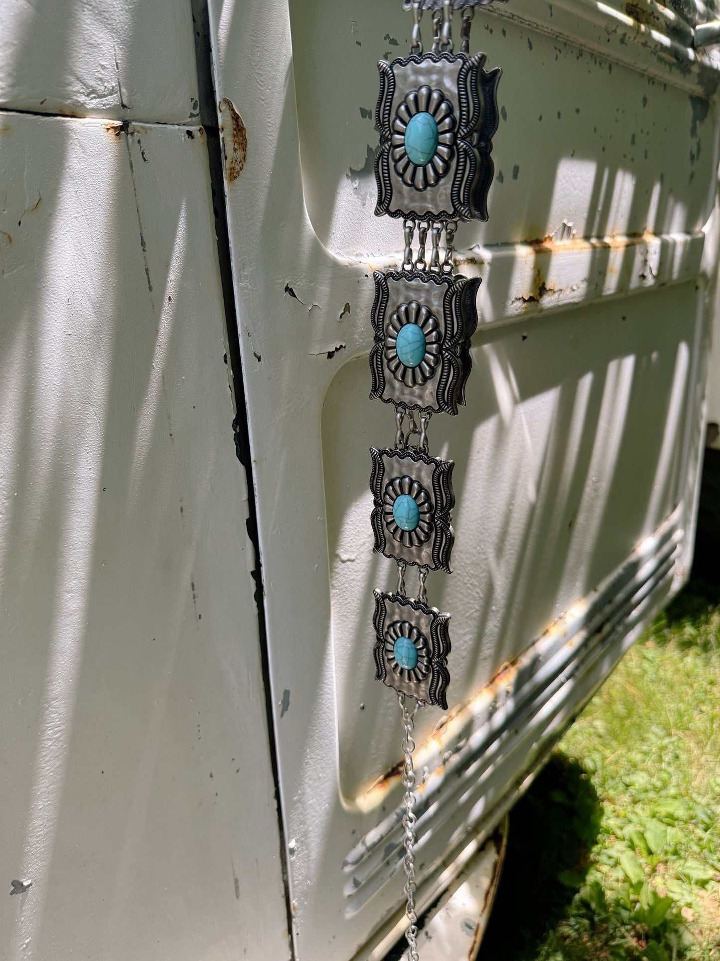 Decorative silver and turquoise earring hanging from a vehicle's rearview mirror.