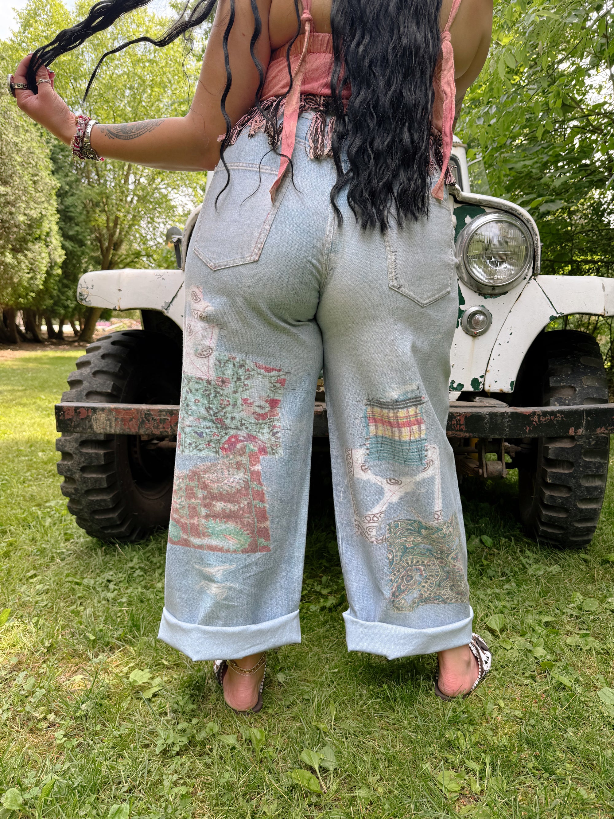 Person wearing patchwork jeans standing in front of a vintage truck in a grassy area.