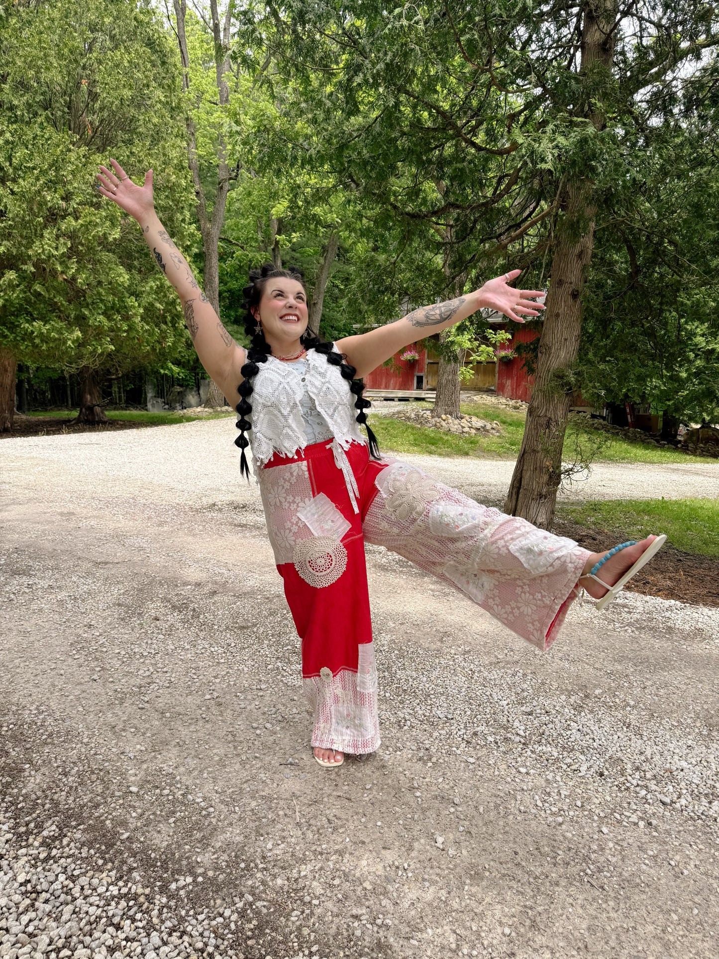 Person in a red and white dress with a black beaded necklace standing on a gravel path with trees in the background.
