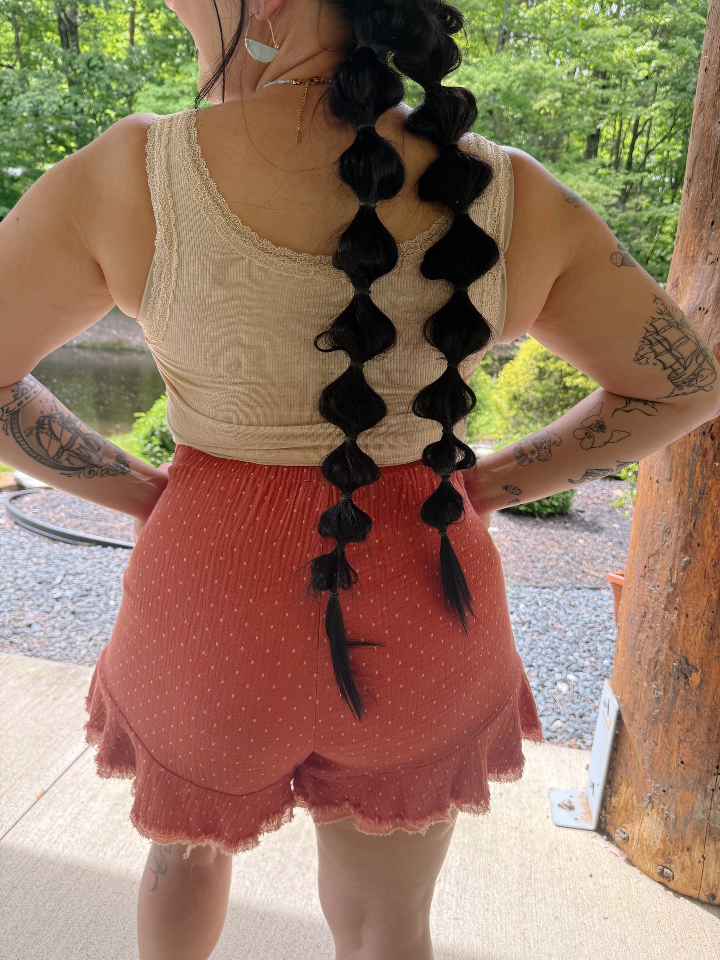 Person wearing a white tank top and pink skirt with black braided hair extensions outdoors.