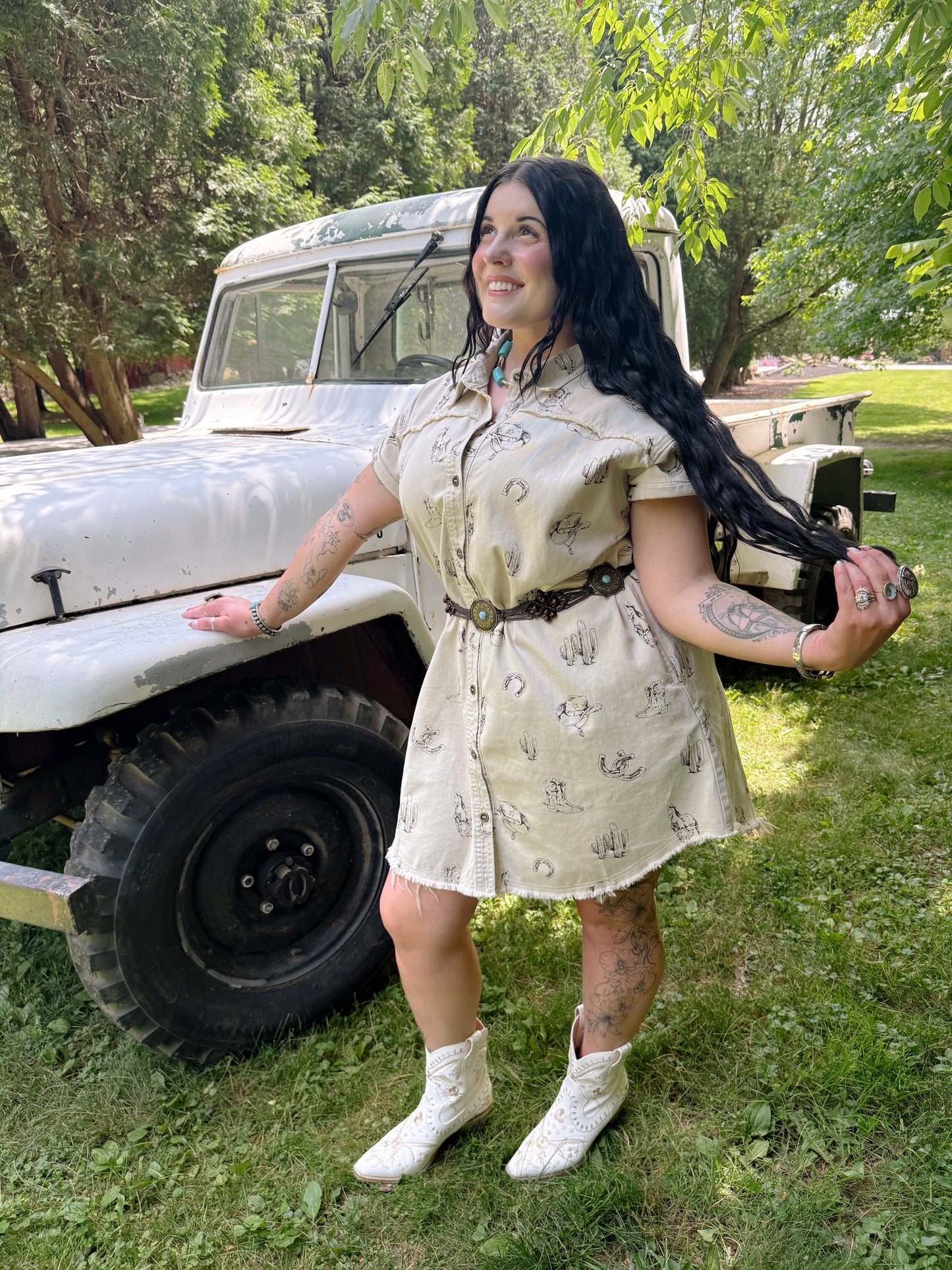 Woman in a beige dress standing in front of a vintage truck with trees in the background